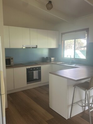 A compact kitchen with white cabinets, a microwave, a kettle, and a sink.