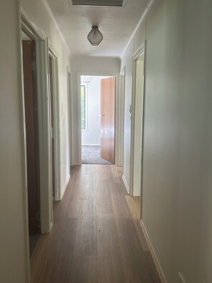 A hallway with wooden flooring, white walls, and doors leading to other rooms.