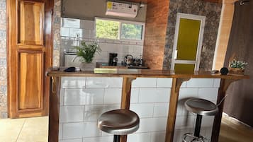 Een keuken met een houten aanrecht, twee barkrukken, een koffiezetapparaat en een raam met uitzicht op groen.
