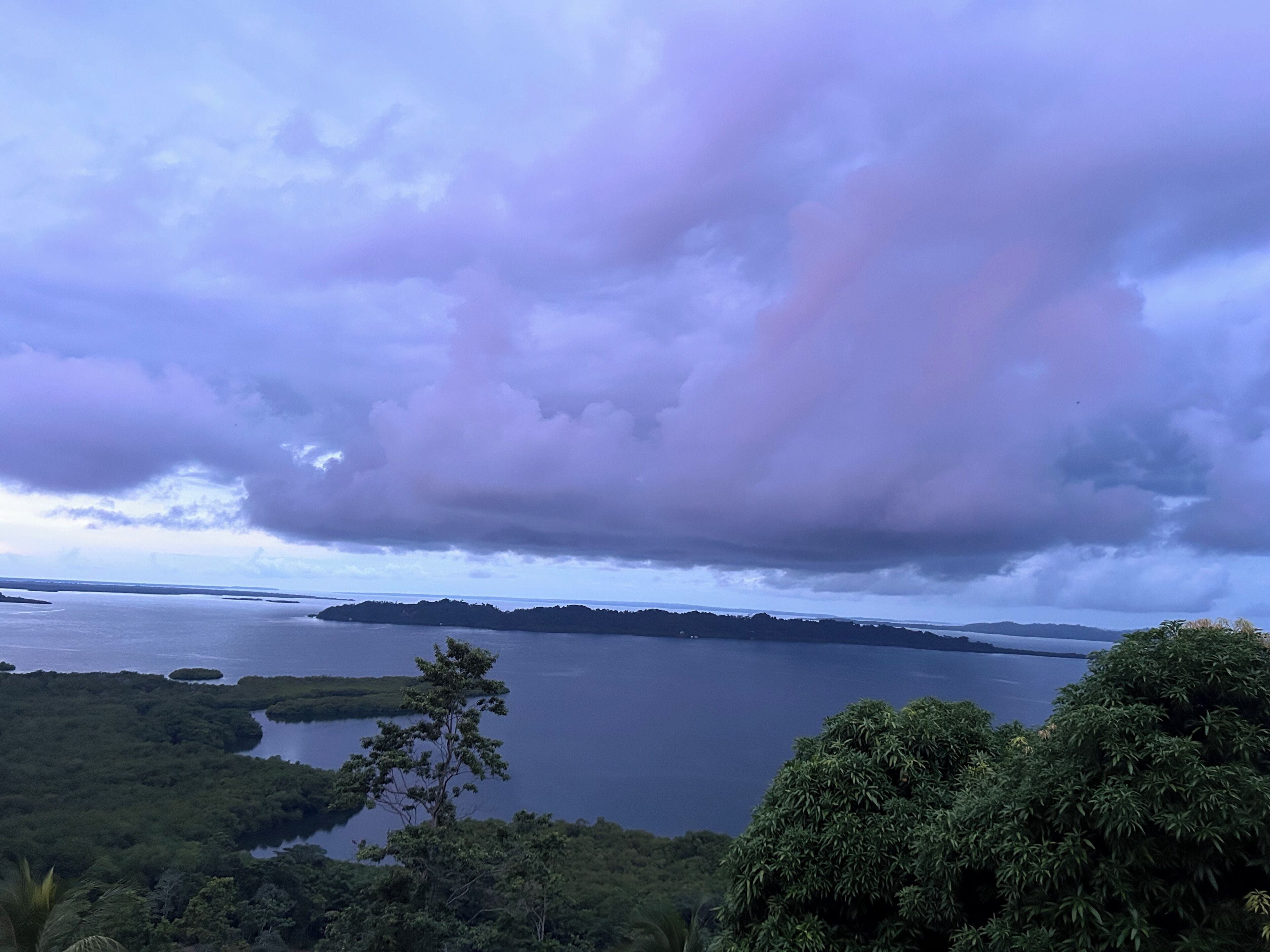 A landscape with a body of water, a distant shoreline, and a cloudy sky.