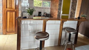 Cocina con encimera de madera, dos taburetes de bar, cafetera y ventana con vista a la vegetación.