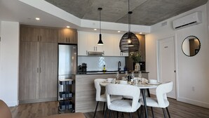 Uma cozinha moderna com frigorífico embutido, área de jantar com mesa redonda e cadeiras brancas, e teto com iluminação embutida.