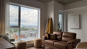 Uma sala de estar moderna com uma janela grande, um sofá de couro marrom e vista para a cidade.