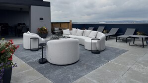 Um terraço no telhado com um sofá seccional, poltronas de descanso e uma área de jantar.