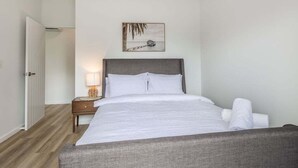 Een slaapkamer met een bed, nachtkastje, lamp en een foto aan de muur.