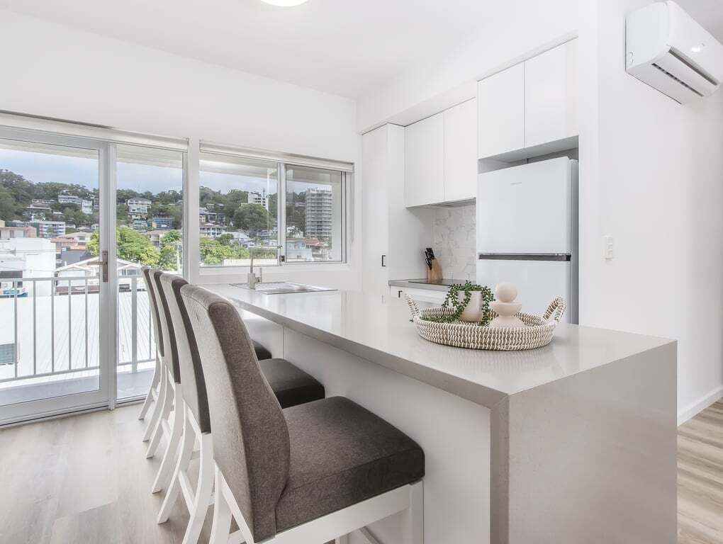 A modern kitchen with a large window, a dining area with chairs, and a small island with decorative items.