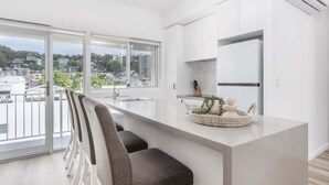 Een moderne keuken met een groot raam, een eethoek met stoelen en een klein schiereiland met decoratieve objecten.