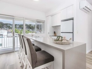 A modern kitchen with a large window, a dining area with chairs, and a small island with decorative items. - The Laneway Villas - Central Apartments in the heart of Burleigh Heads - Unit 3 (Gold Coast)