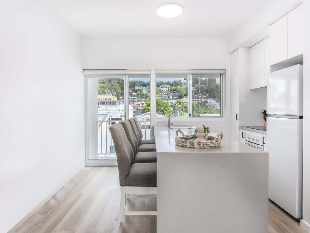 A modern kitchen with a large island, white cabinets, and a view of a cityscape through large windows.