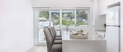 A modern kitchen with a large island, white cabinets, and a view of a cityscape through large windows.
