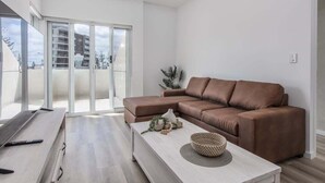 Een moderne woonkamer met een bruine leren bank, een witte salontafel en een schuifdeur naar een balkon.