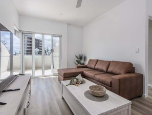 A modern living room with a brown leather sofa, a white coffee table, and a sliding glass door leading to a balcony. - The Laneway Villas - Central Apartments in the heart of Burleigh Heads - Unit 3 (Gold Coast)