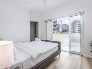 A bedroom with a bed, a nightstand, a lamp, and a sliding glass door leading to an outdoor balcony. - The Laneway Villas - Central Apartments in the heart of Burleigh Heads - Unit 3 (Gold Coast)