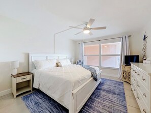 Une chambre à coucher comprenant un lit, une table de chevet, une commode, un téléviseur et un ventilateur de plafond.