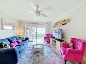 A living room with a sofa, armchairs, a coffee table, a TV, and a ceiling fan. - Ocean View Beach Condo w/ Heated Pool in Cocoa Beach (Cocoa Beach)