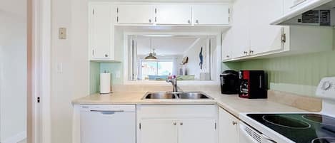 Une cuisine moderne avec des meubles blancs, un lave-vaisselle, un évier, une cuisinière et une machine à café.