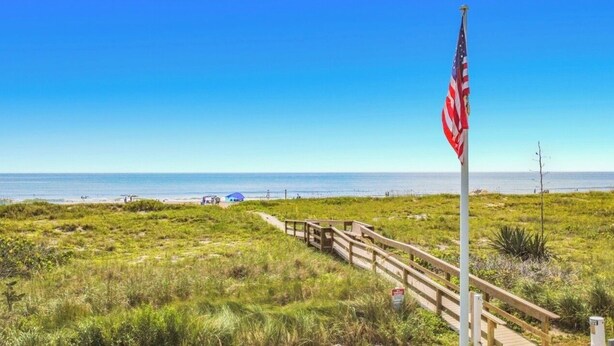 A beach with a wooden boardwalk leading to a flagpole with an American flag. - Ocean View Beach Condo w/ Heated Pool in Cocoa Beach (Cocoa Beach)