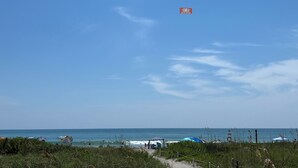 A beach with umbrellas, a path, and a sign in the distance. - Ocean View Beach Condo w/ Heated Pool in Cocoa Beach (Cocoa Beach)