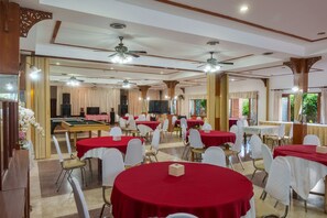A banquet hall with multiple round tables covered in red tablecloths, white chairs, and ceiling fans.