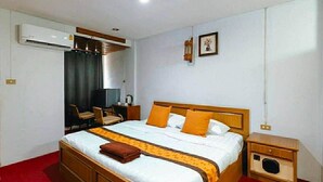Una habitación de hotel con una cama de madera, un escritorio, una silla, un equipo de aire acondicionado y un mueble pequeño.