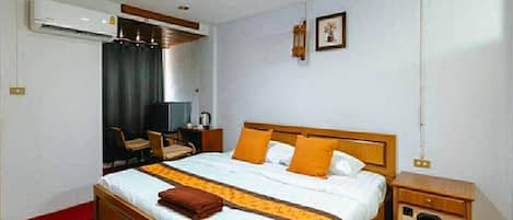 Una habitación de hotel con una cama de madera, un escritorio, una silla, un equipo de aire acondicionado y un mueble pequeño.