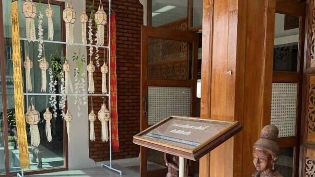 Un área de recepción con una estatua de madera, un expositor y una vitrina de vidrio con objetos colgantes.