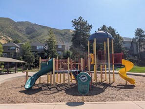 Ein Spielplatz mit Rutschen und Klettergerüsten, umgeben von einem Park mit Picknicktisch und Laube.
