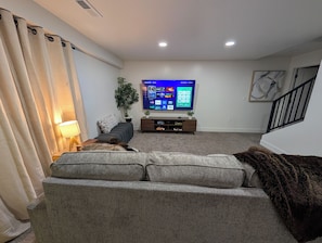 Ein Wohnzimmer mit einer Couch, einem Fernseher, einer Pflanze und einer Treppe.