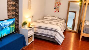 Ein Schlafzimmer mit einem Bett, einem Fernseher, einem Nachttisch mit Lampe, einem Wandbehang im Traumfänger-Stil und einem Spiegel.