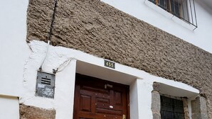 Un edificio con fachada de piedra, una puerta de madera con placa de número y una maleta negra en los escalones.