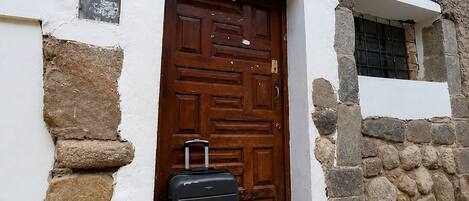 A building with a stone facade, a wooden door with a number plate, and a black suitcase on the steps.