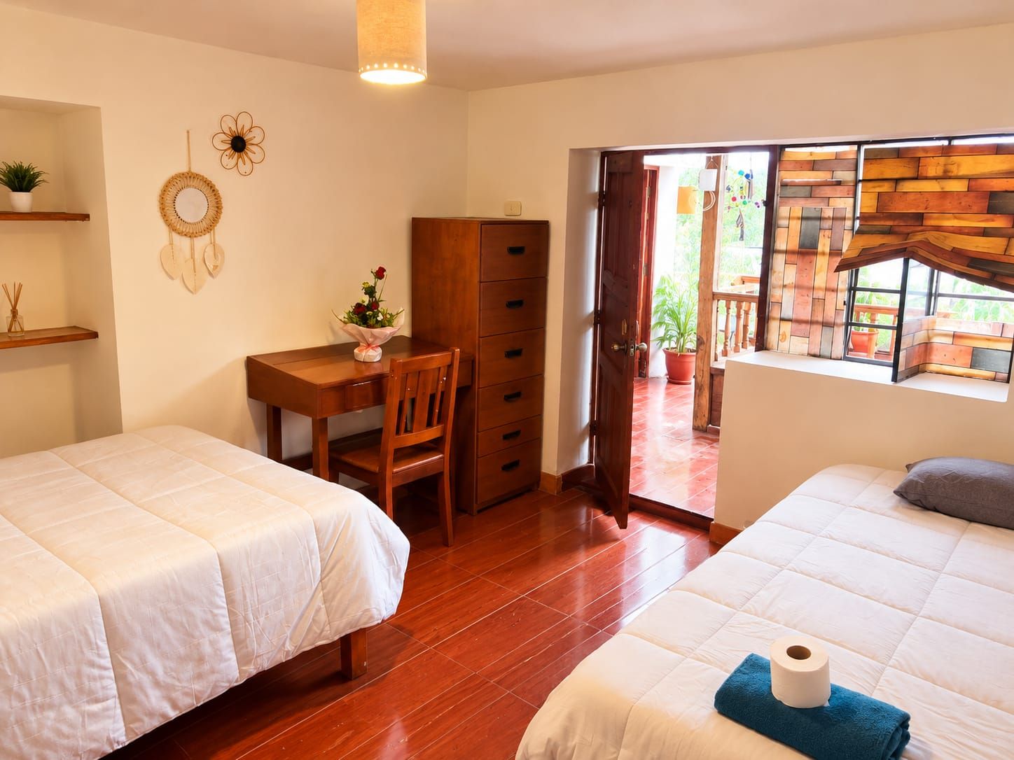 A bedroom with two beds, a desk with a chair, a wardrobe, and a window with a view of the outside.