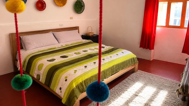 Un dormitorio con una cama, una mesita de noche, una ventana con cortinas rojas y adornos en la pared.