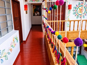A hallway with a wooden railing decorated with colorful balls, a red floor, and a door with a window. - Delight Peru Backpackers (Cusco)