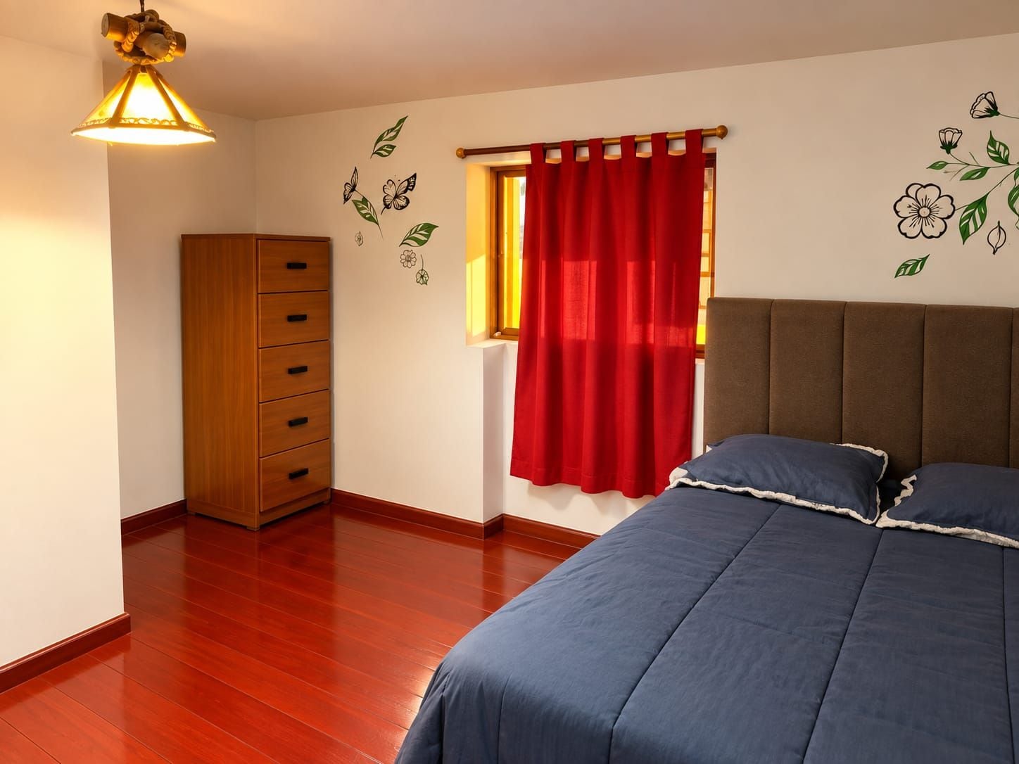 Ein Schlafzimmer mit einem Bett, einem Kleiderschrank, einem Fenster mit roten Vorhängen und Wandstickern.