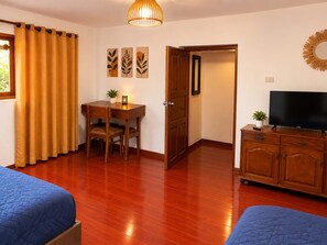 A hotel room with a wooden desk, two beds, a television, and a door leading to another room. - Delight Peru Backpackers (Cusco)