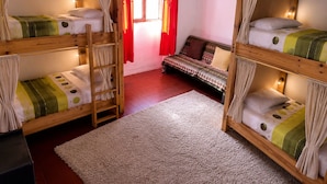 Un dormitorio con literas, un sofá pequeño y una ventana con cortinas rojas.