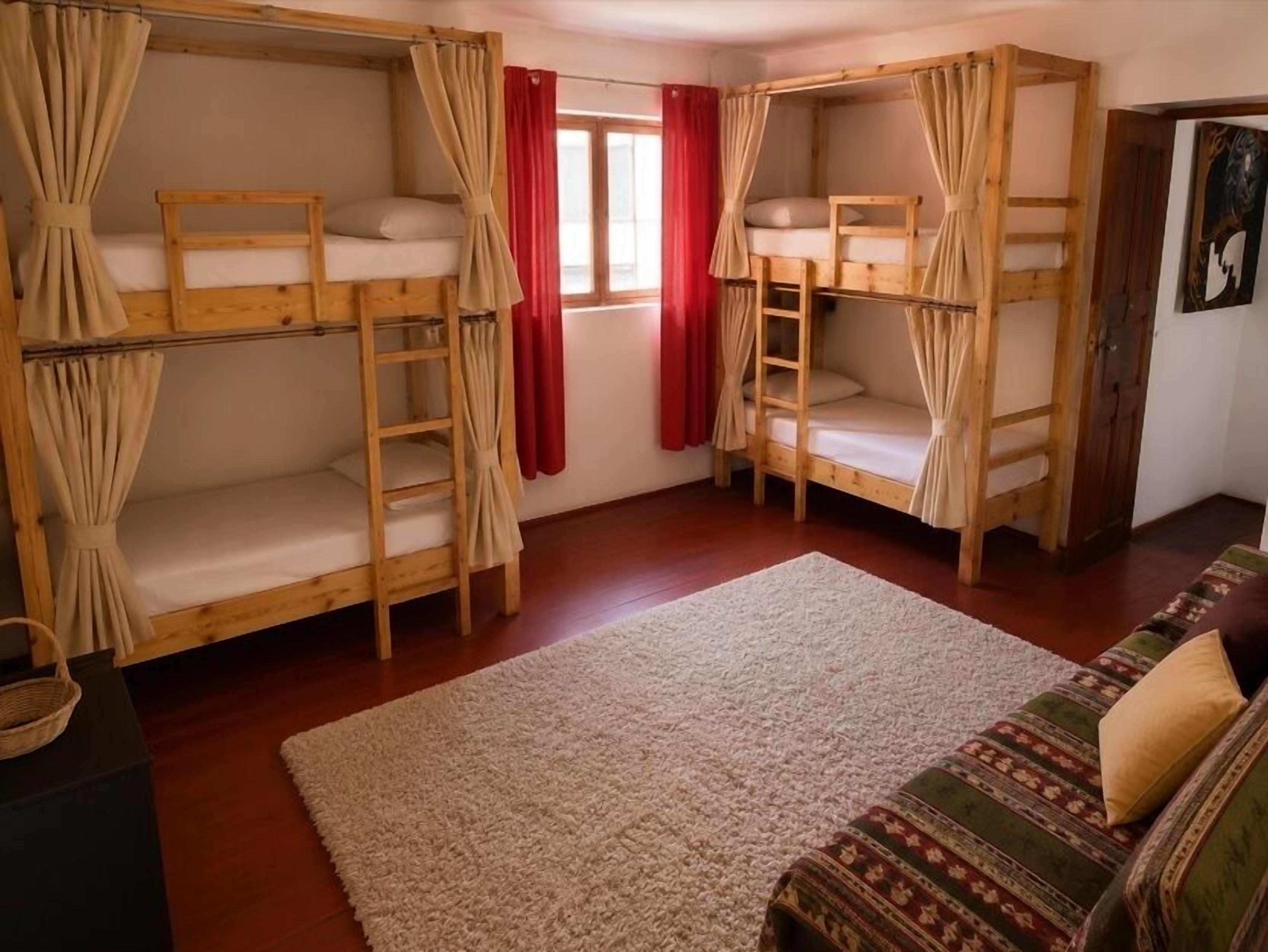 A room with bunk beds, a sofa, a window with red curtains, and a carpeted floor.
