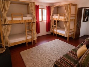 A room with bunk beds, a sofa, a window with red curtains, and a carpeted floor. - Delight Peru Backpackers (Cusco)