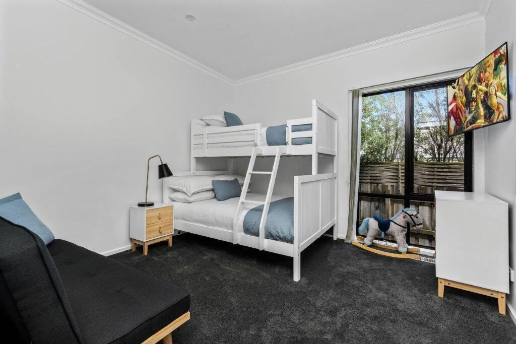 A bunk bed room with a desk, a chair, and a window with a view of trees.
