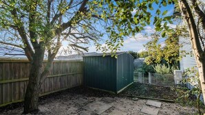 Un patio trasero con una cerca de madera, un cobertizo y un árbol.