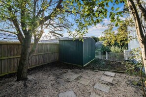 Ein Garten mit Holzzaun, Gartenhaus und Baum.