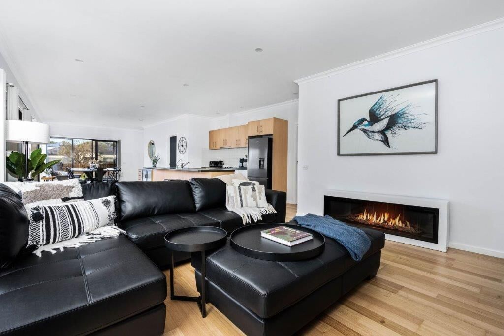 Una sala de estar moderna con un sofá de cuero negro, una chimenea y un comedor al fondo.