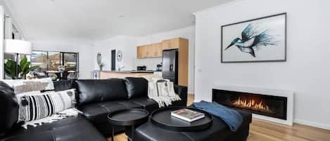 Una sala de estar moderna con un sofá de cuero negro, una chimenea y un comedor al fondo.