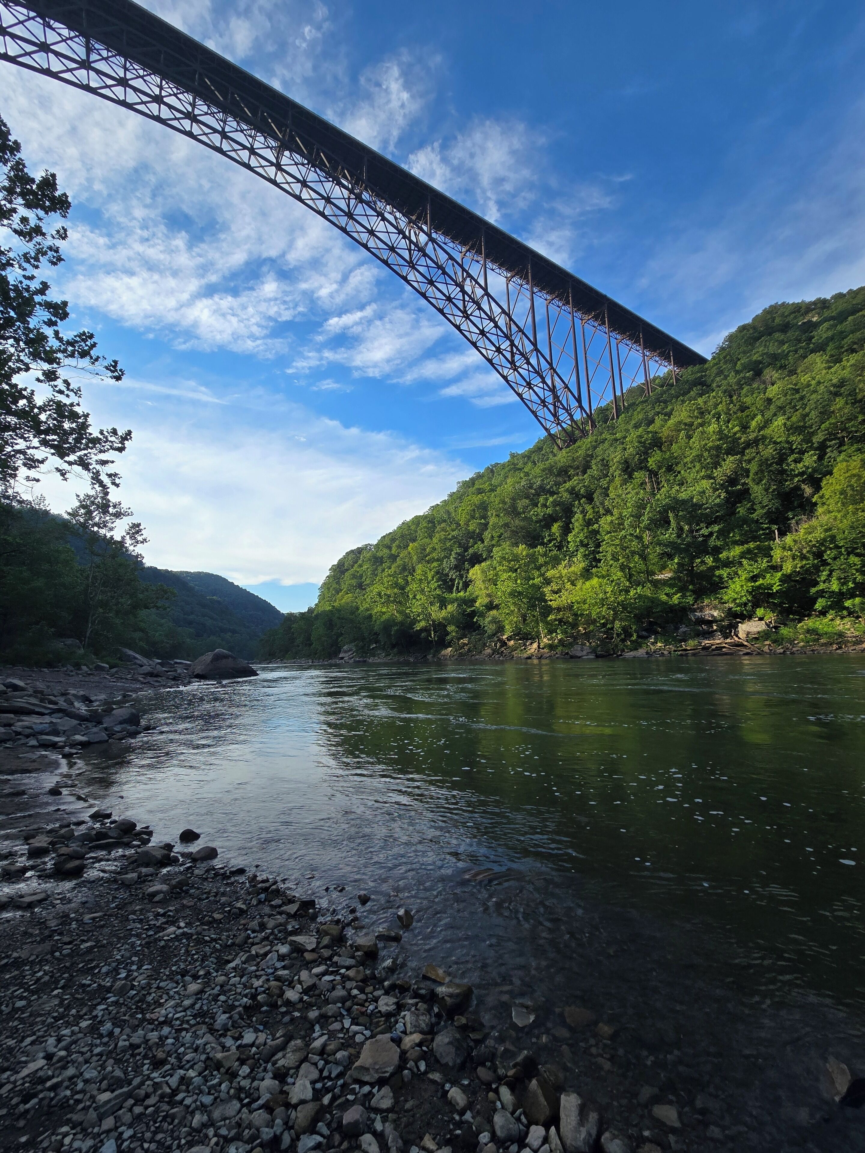A river with a bridge, surrounded by greenery and hills.
