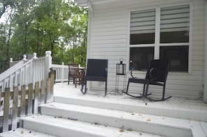A porch with steps leading to a white house, a rocking chair, a table, and a lantern.