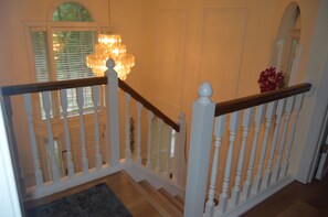 A staircase with white balusters and a wooden handrail, leading to a room with a chandelier and a window with blinds. - Mountain-Top HOUSE with a Pool, Near Potomac River Beach! in serene Stafford (Stafford)