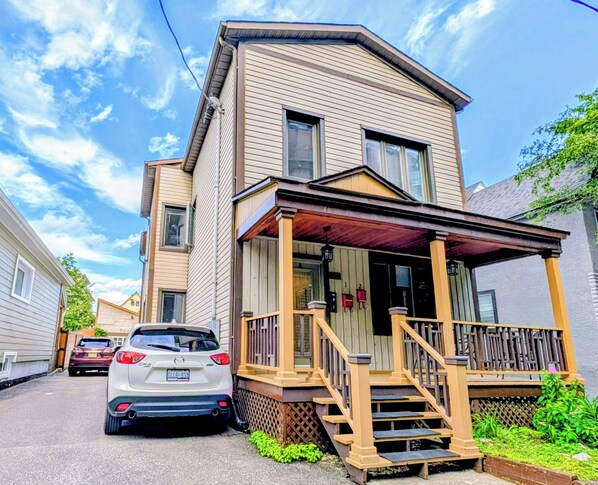 A two-story residential building with a front porch and a car parked in front.