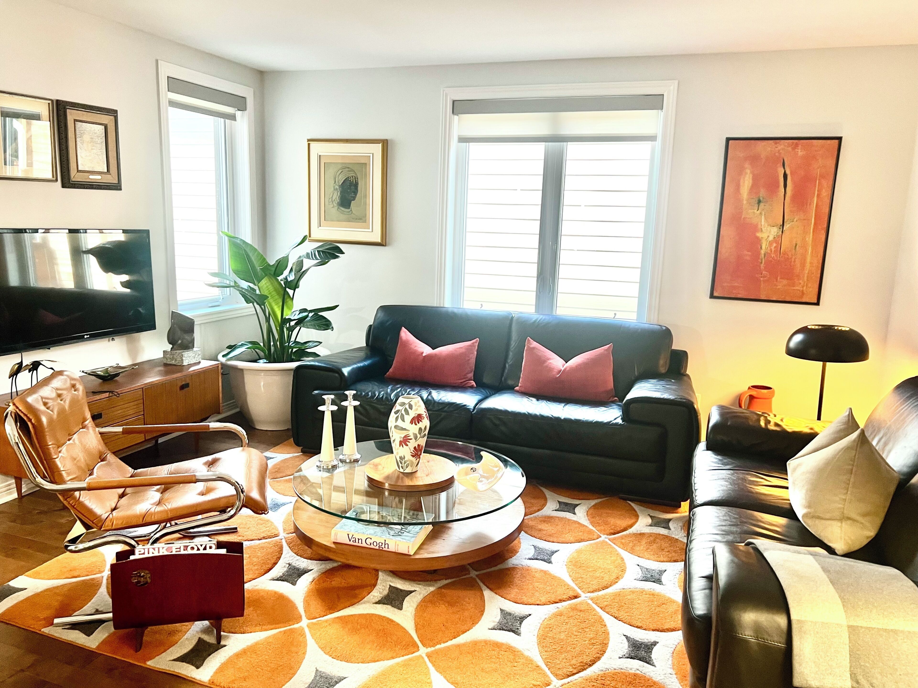 Un salon avec un canapé en cuir, une table basse en verre sur laquelle repose un livre, un téléviseur et une plante en pot.
