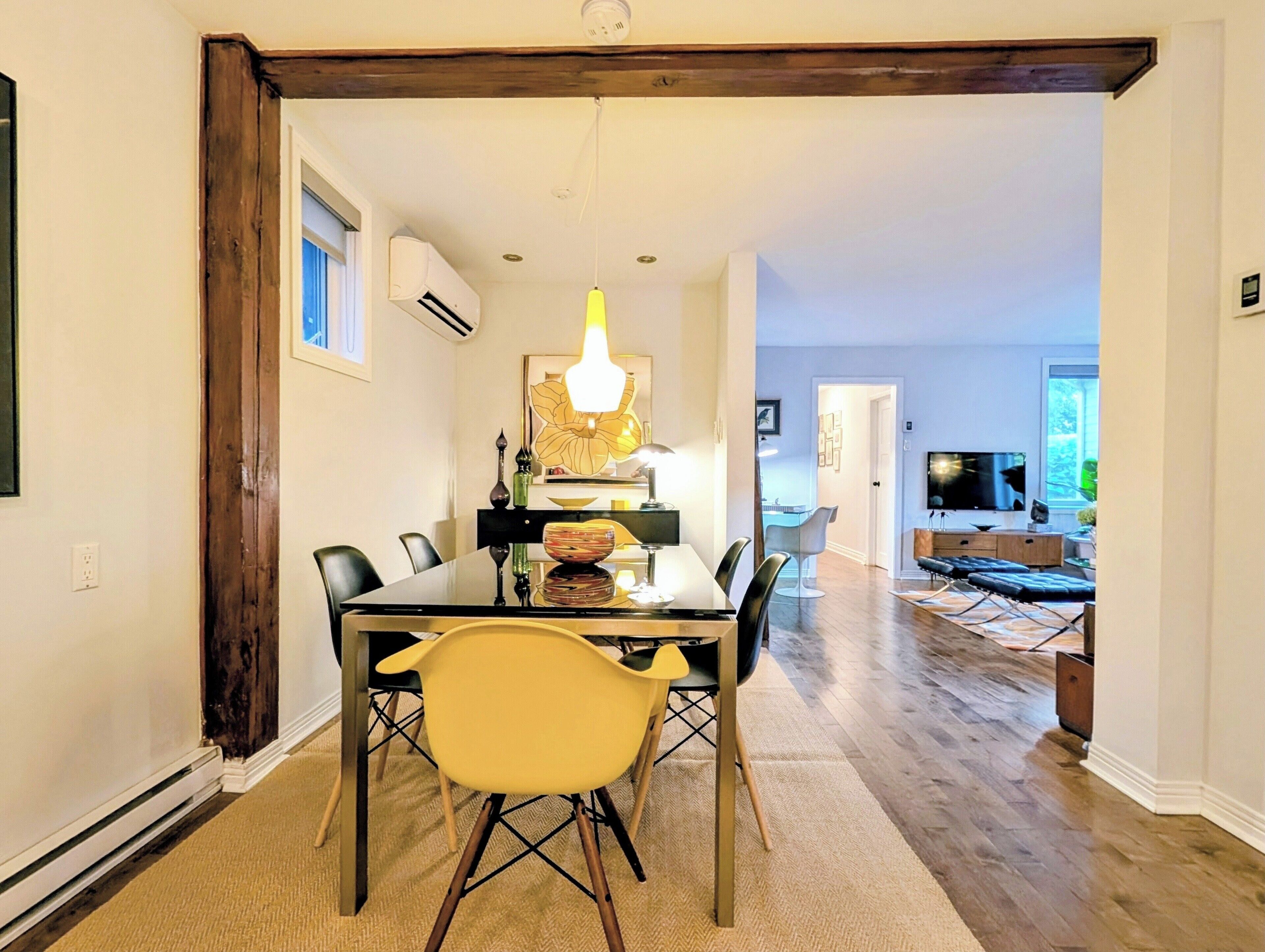 A dining area with a glass table, chairs, and a chandelier. There is a television in the background.
